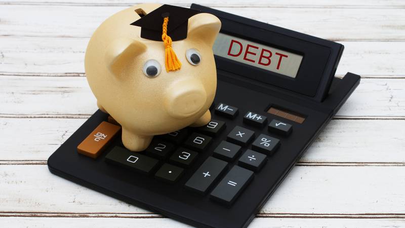 Calculating your student loan debt, A golden piggy bank with a grad hat on a calculator with word Debt over a distressed wood background